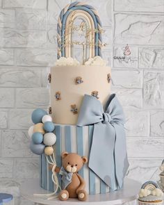 a three tiered cake with a teddy bear on the side and balloons around it