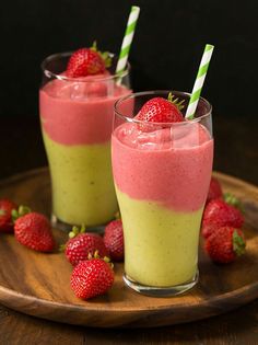 a smoothie in a glass with strawberries on the side and another one behind it