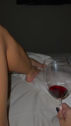 a person holding a wine glass with red liquid in it on top of a bed