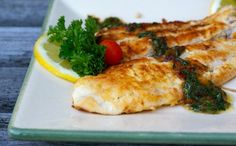 two fish fillets on a plate with lemon wedges and parsley garnish