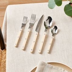 four forks, two spoons and one knife on a table with a plant in the background