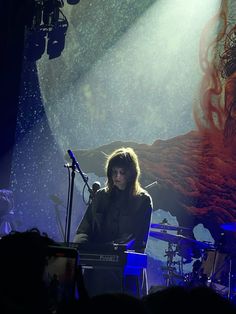 a woman standing in front of a microphone on top of a stage with other people