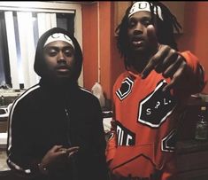 two young men standing next to each other in a room with orange walls and cabinets