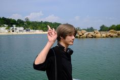 a young man standing on top of a boat in the water holding his hand up