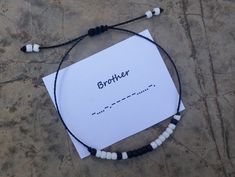 a bracelet that says brother on it sitting on the ground next to a piece of paper