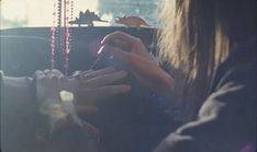 a woman sitting in the back seat of a car with her hands on a beaded necklace