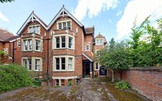 a large brick building with lots of windows on the front and side of it, surrounded by greenery