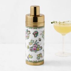 a drink in a glass next to a floral print cocktail shaker with a gold rim