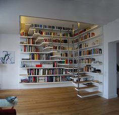 a living room filled with lots of books on shelves next to a stair case full of books