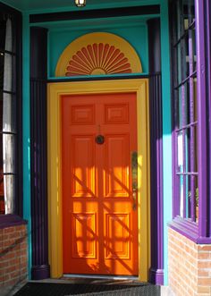 an orange and yellow door is in front of a brick building with purple trimming