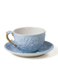 a blue cup and saucer sitting on top of a white plate with gold trim