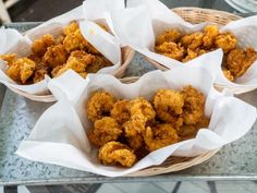 four baskets filled with fried food sitting on top of a glass table covered in paper