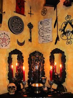 a table with candles and skulls on it in front of a wall decorated with various items