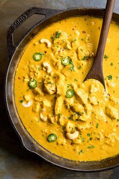 a skillet filled with yellow curry and chicken, topped with cashews on the side