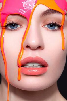 a woman's face with orange and pink paint dripping on her cheek, as if it were melted