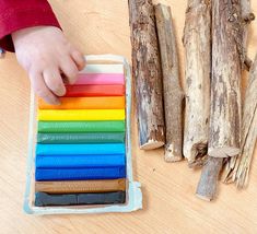 a child is playing with colored sticks on the table next to it are wood logs