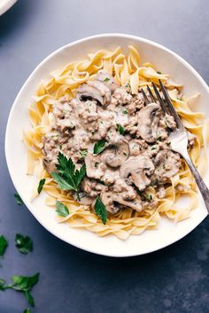 a white bowl filled with pasta covered in mushroom sauce and garnished with parsley