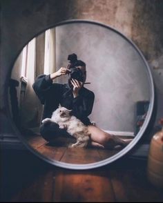 a woman taking a selfie in front of a mirror with her cat sitting on the floor