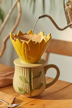 a yellow coffee cup sitting on top of a wooden table next to a metal spoon