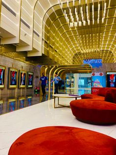 people are walking through an airport lobby with red couches and large chandeliers hanging from the ceiling