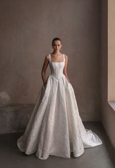 a woman in a white wedding dress standing by a window