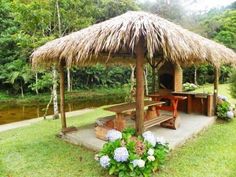 a gazebo made out of wood and grass with flowers in the foreground