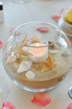 a glass bowl filled with sand and seashells on top of a white table