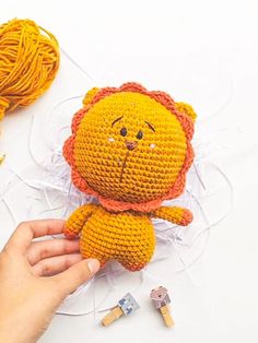 a hand holding a small stuffed animal next to some yarn and crochet hooks