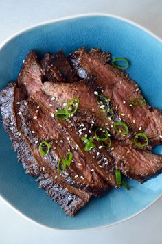 a blue plate topped with steak covered in sesame seeds and garnished with green onions