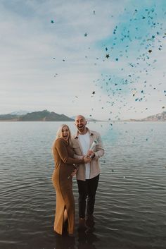 a man and woman standing in the water with confetti falling from the sky