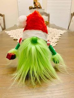 a green hairy toy with a santa hat on it's head sitting on top of a wooden table