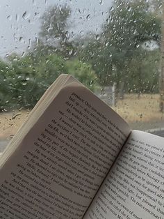 an open book sitting on top of a window sill next to rain covered windows