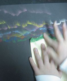 a person's hand on top of a piece of paper with colorful lines in the background