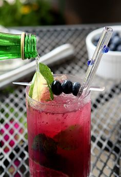 a glass filled with blueberries and limeade sitting on top of a metal table