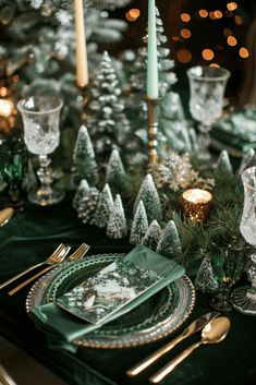 a table set for christmas dinner with green and gold plates, silverware and candles