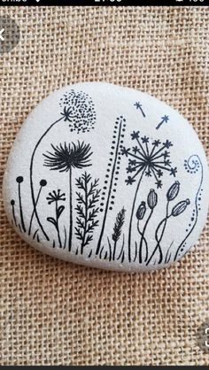 a painted rock sitting on top of a piece of burlocked fabric with dandelions and other plants