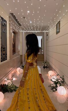 a woman in a long yellow dress walking down a hallway with lights on the ceiling