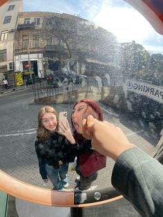 two women taking a selfie in front of a parking sign with the reflection of another woman's face