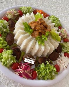 a white plate topped with meatballs and veggies on top of rice covered in sauce