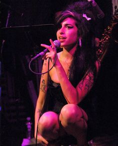 a woman with tattoos on her arms and legs, kneeling down while holding a microphone