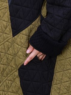 a person's hand on the back of a quilted green and black jacket