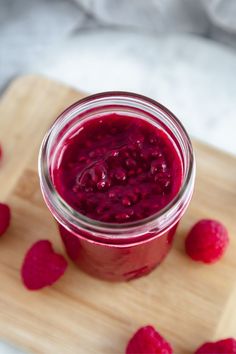 a jar filled with raspberry jam on top of a wooden cutting board