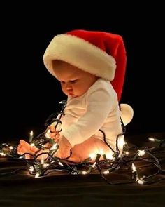 a baby wearing a santa hat sitting on top of a bed covered in christmas lights