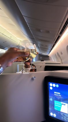 two people toasting wine glasses on an airplane with the entertainment system in the background