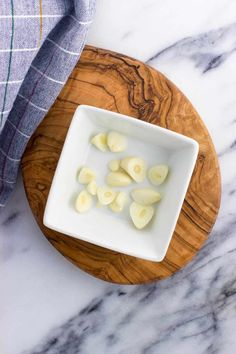 peeled potatoes in a white bowl on a wooden cutting board next to a blue checkered dish towel