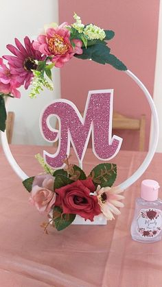 a pink table topped with a white cake plate covered in flowers and the letter m