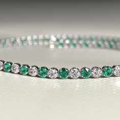 an emerald and diamond tennis bracelet on a white surface with diamonds around the perimeters