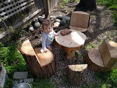 a toddler sitting on top of a wooden stump table next to two chairs and a tree stump