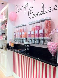 the candy shop is decorated with pink and white striped walls, black countertop, and shelves filled with candies