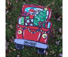 a red car with presents in the back on top of it sitting in leaves and grass